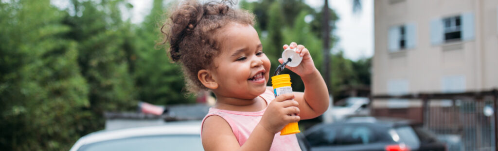 Criança sorrindo enquanto brinca de fazer bolhas de sabão ao ar livre