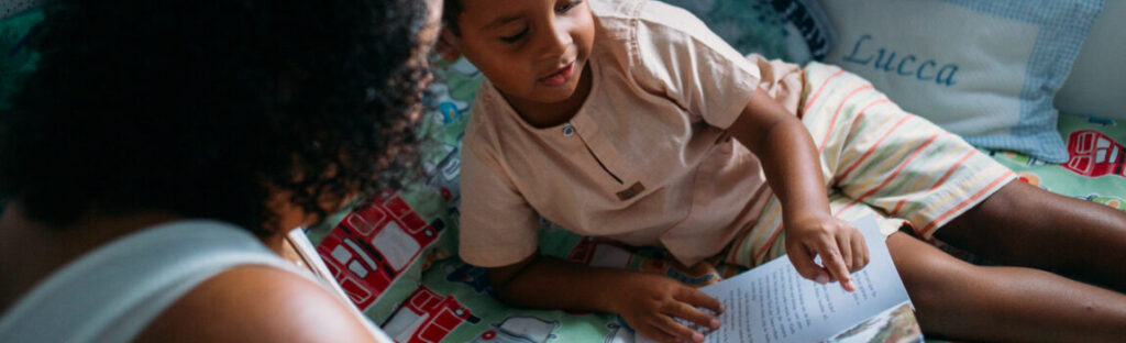 Uma mãe lê para seu filho, que segura um livro deitado na cama. Ilustra matéria de campanha de distribuição de livros realizada pela Fundação Maria Cecilia Souto Vidigal e Instituto Mauricio de Souza.